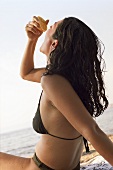 Young woman on beach squeezing an orange into her mouth