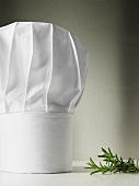 A chef's hat, rosemary beside it