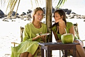 Zwei Freundinnen mit Wassermelone und Kokosmilch am Strand