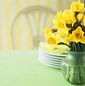 Vase mit Narzissen und Tellerstapel auf einem Tisch