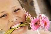 Young woman with pink gerberas in her mouth