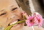 Junge Frau mit drei rosa Gerbera im Mund