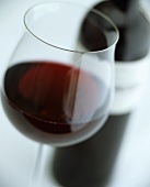 Glas Rotwein mit Rotweinflasche im Hintergrund