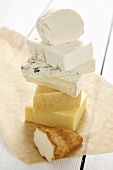 Pieces of different cheeses, stacked on paper