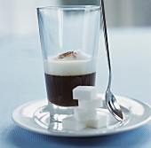A glass of espresso macchiato, sugar