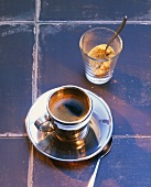 Espresso in silver cup and saucer with brown sugar on tiles