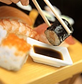 Hand taucht Maki-Sushi in Sojasauce