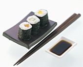 Drei Maki-Sushi mit Stäbchen und Sojasauce
