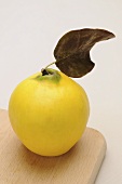 A quince with a leaf on a chopping board