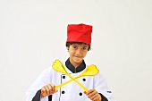 A boy dressed as a chef holding salad servers