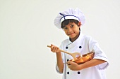 A boy dressed as a chef holding a mixing bowl and a wooden spoon