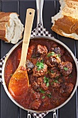 Pot of Homemade Meatballs in Sauce with Parsley; Wooden Spoon; Bread