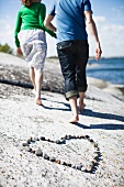 A couple walking away from a pebble heart on a rocky beach