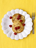Two Pancakes with Fresh Raspberries on a White Plate; Yellow Background