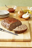 Partially Sliced Meatloaf on Cutting Board; Plates and Ingredients
