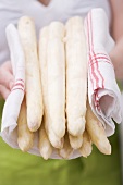 A woman holding white asparagus in a tea towel