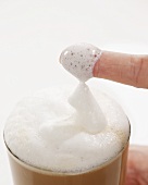 Milk foam covered finger from a glass of Latte Macchiato