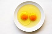 Zwei aufgeschlagene rohe Eier auf Teller (Draufsicht)