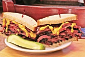Halved Large Pastrami Sandwich with Mustard and a Pickle