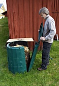 Mann öffnet gefüllte Komposttonne