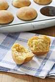 Corn Muffin Halved on a Dish Towel; Muffins in Baking Tin