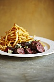 Sliced Steak with Blue Cheese and French Fries on a White Plate