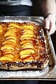 Hands holding a peach tart on a baking tray