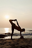 A woman practicing yoga on a beach at sunset