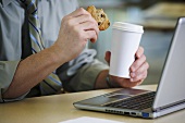 A man at a desk with coffee and a cookie
