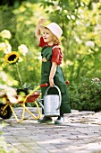 A little girl dressed as a gardener holding a watering can and a sunflower