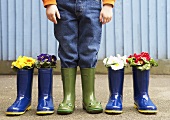 A boy wearing wellies standing between wellies filled with flowers