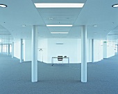 Weitläufiger, leerer Raum mit grauem Teppichboden, Säulen und einem zentralen Arbeitsplatz