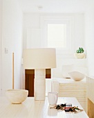 Weisser Holztisch mit cremefarbener Tischlampe und Kerzenschale, Teetasse und Schlüsselbund