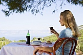 A woman sitting at a table with a glass of wine looking out to sea