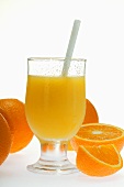 Orange juice in glass with straw; fresh oranges