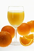 Cold orange juice in stemmed glass; orange wedges & oranges