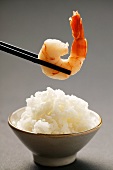 Shrimp on chopsticks above bowl of rice