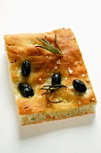 Piece of focaccia with olives, salt and rosemary