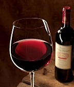 Glas Rotwein vor Rotweinflasche