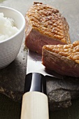 Fried duck breast, a piece cut off, on knife, rice