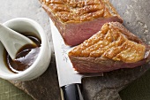 Fried duck breast, a piece cut off, on knife, soy sauce