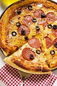 Pizza with salami, cheese and olives, a piece cut