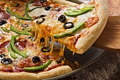 Pizza mit Käse, Salami, Paprika und Oliven, angeschnitten