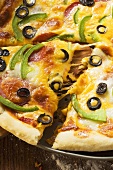 Pizza with cheese, salami, peppers and olives, a piece cut