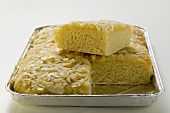 Bee sting cake with flaked almonds in baking tin, partly sliced