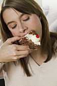 Young woman biting into piece of cream cake
