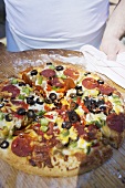 Hands holding pepperoni pizza with peppers and olives