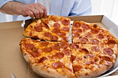 Hand nimmt Stück Peperoniwurst-Pizza aus Pizzakarton