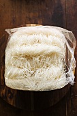 Thin rice noodles in plastic bag on wooden plate