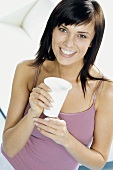 Junge Frau mit einem Becher Trinkjoghurt und 'Milchbart'